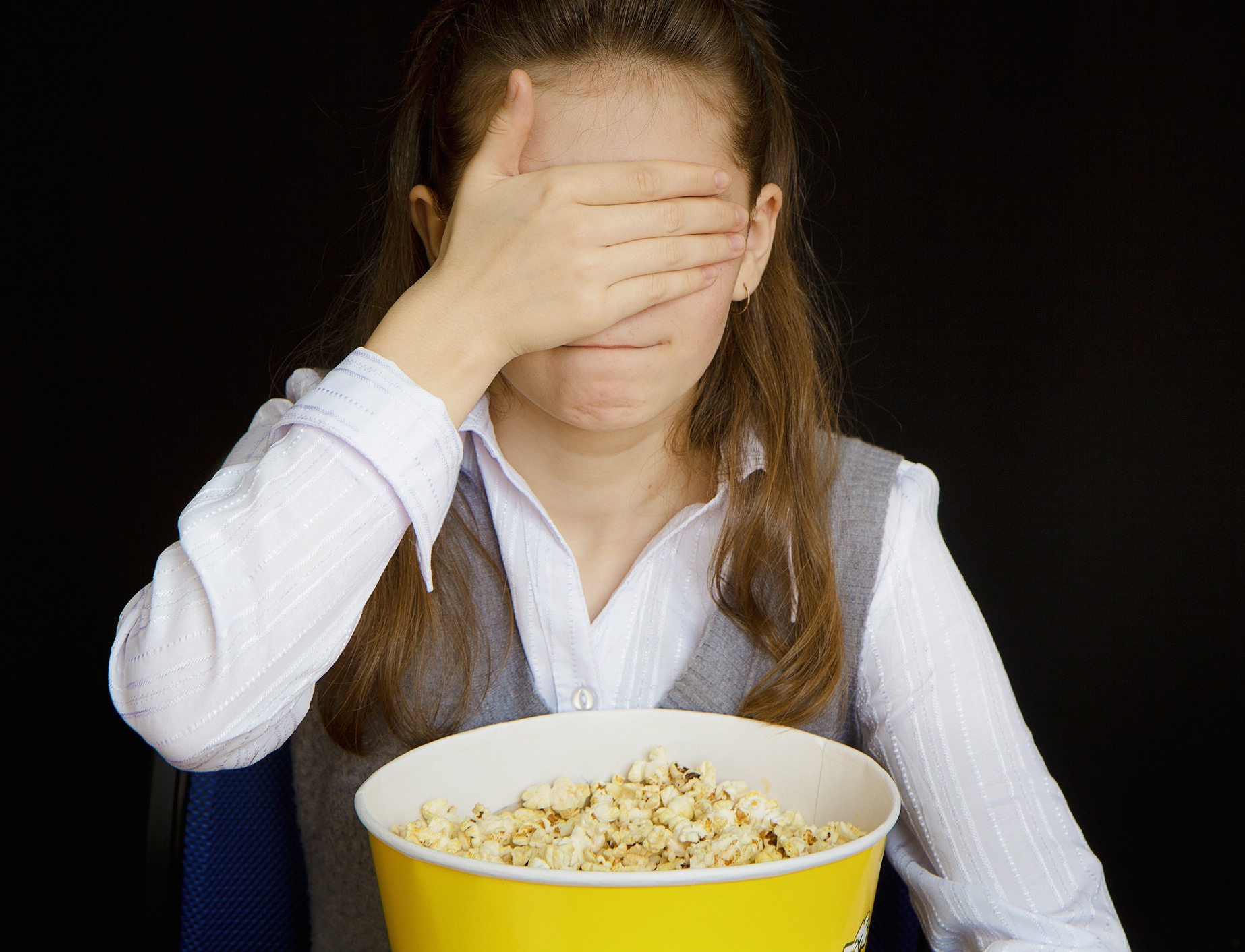 girl with popcorn covering her eyes with her hand